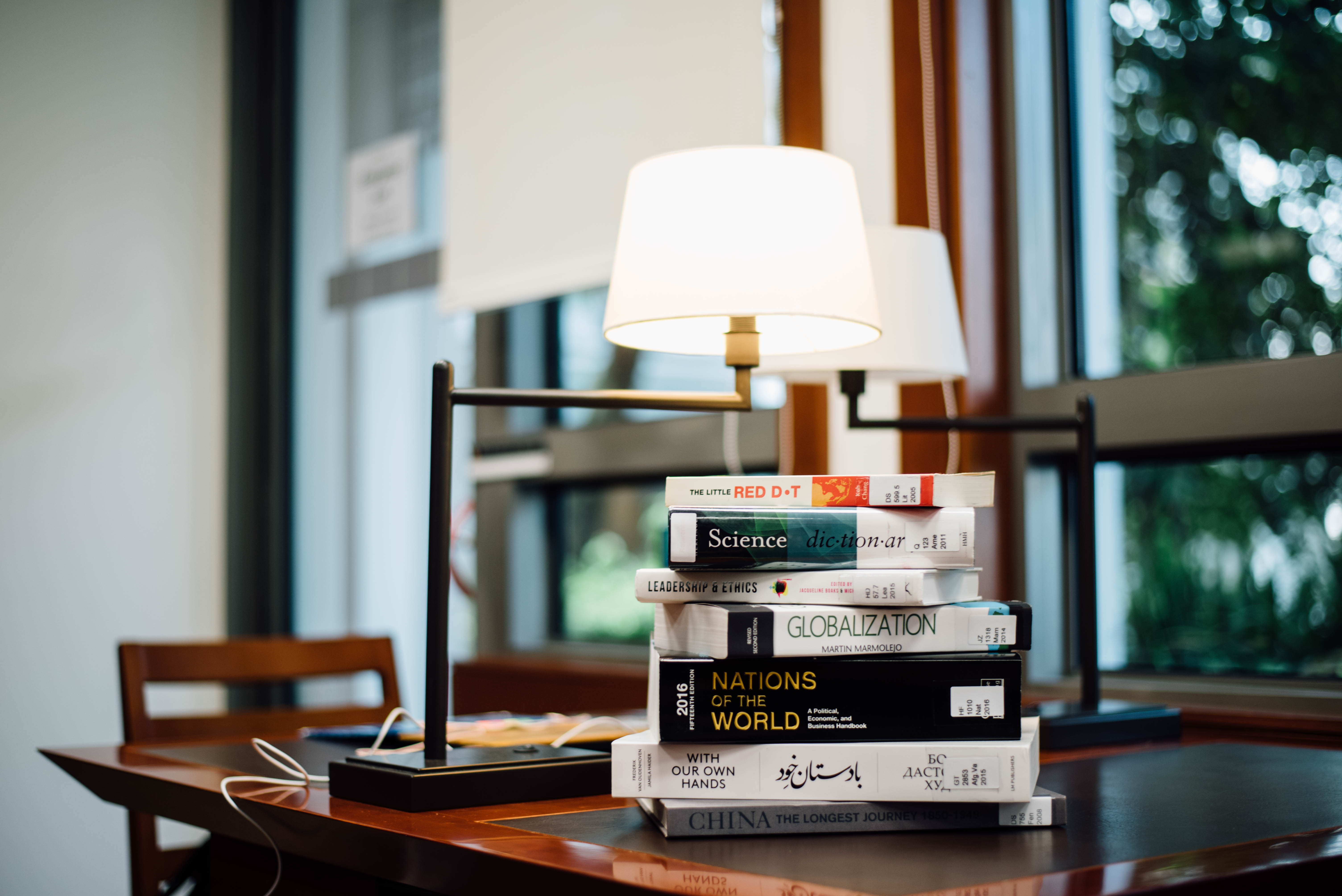 Stack of hardback books on a dim desk under twin lamps — the analog version of a team wiki.