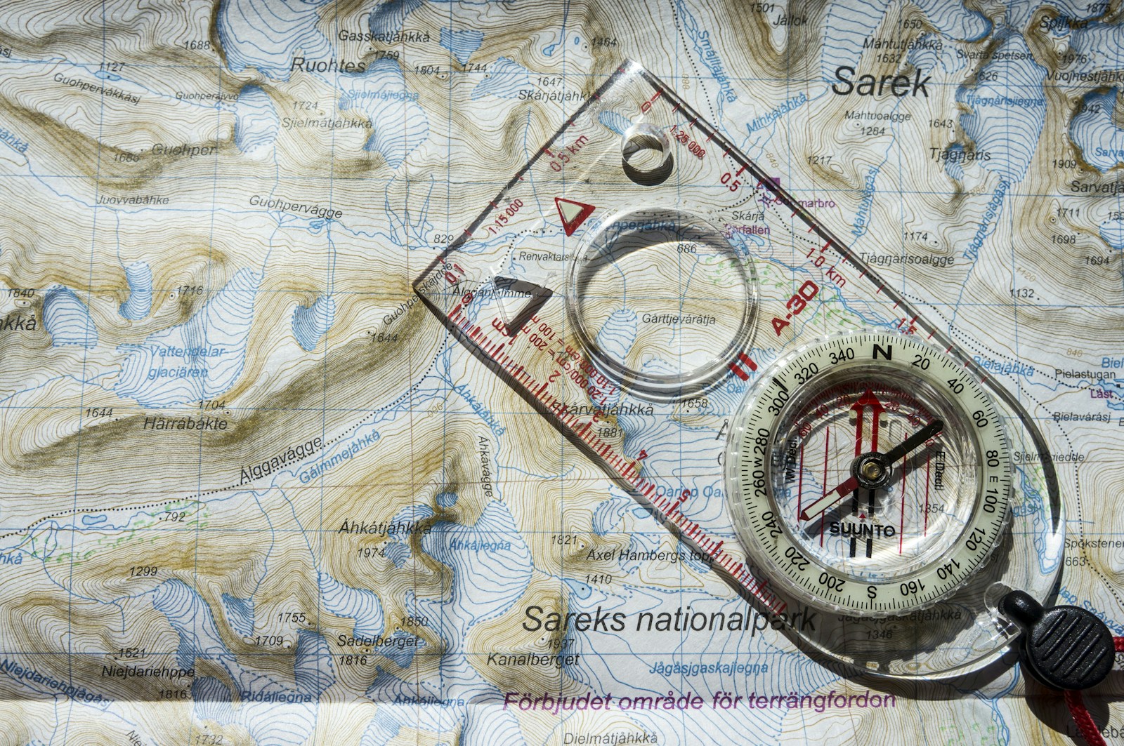 Paper topographic map with a clear compass and ruler resting on top, photographed at Sarek National Park.